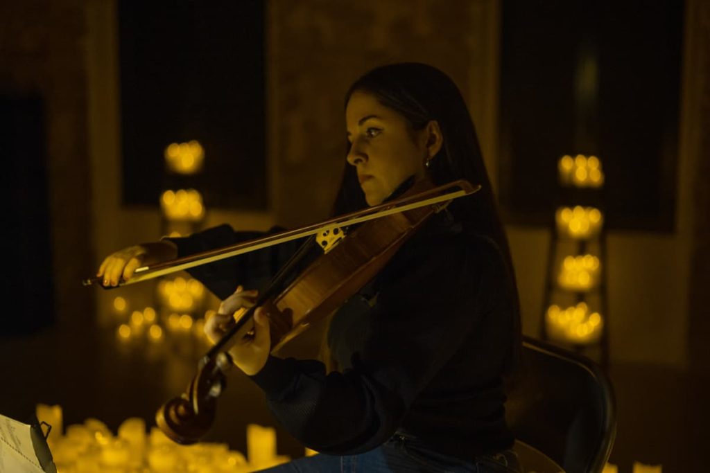 Une violoniste joue pour un concert Candlelight un morceau au violon entourée de bougies