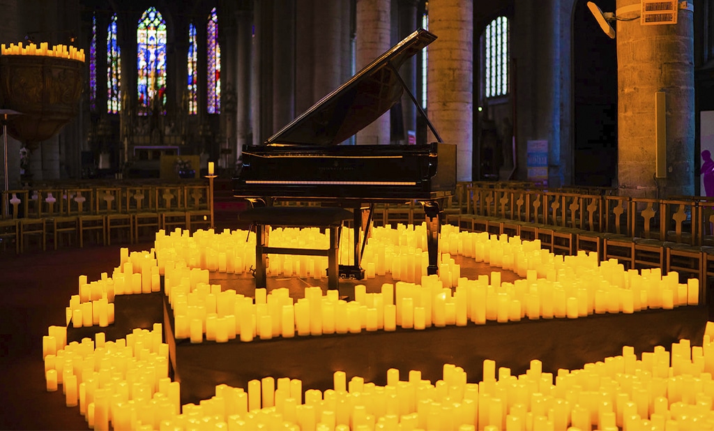 Concert Candlelight dans l'Eglise Saint-Maurice avec les vitraux en fond, les bougies qui entourent le piano à queue noir posé sur l'estrade au milieu de la structure de pierre de l'édifice.