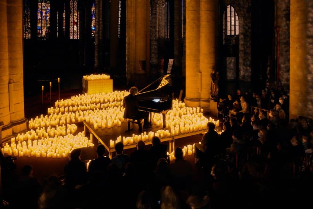 La photo montre un concert Candlelight dans l'Eglise Saint-Maurice à Lille au piano, avec un homme jouant au milieu de l'édifice entouré de lumières de bougies par dizaines.