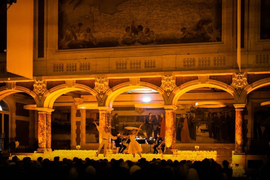 Concert Candlelight au Palais de la bourse à Lille. Scène carrée entourée de bougies sous les arches de la salle avec des musiciens et une danseuse.